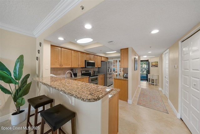 kitchen with light stone countertops, ornamental molding, kitchen peninsula, appliances with stainless steel finishes, and light tile floors