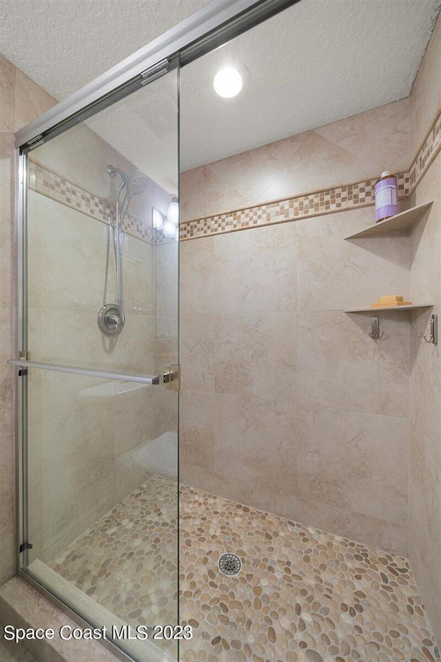 bathroom with a shower with shower door and a textured ceiling