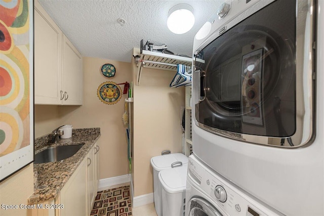 laundry area featuring cabinets, a textured ceiling, stacked washing maching and dryer, sink, and light tile floors