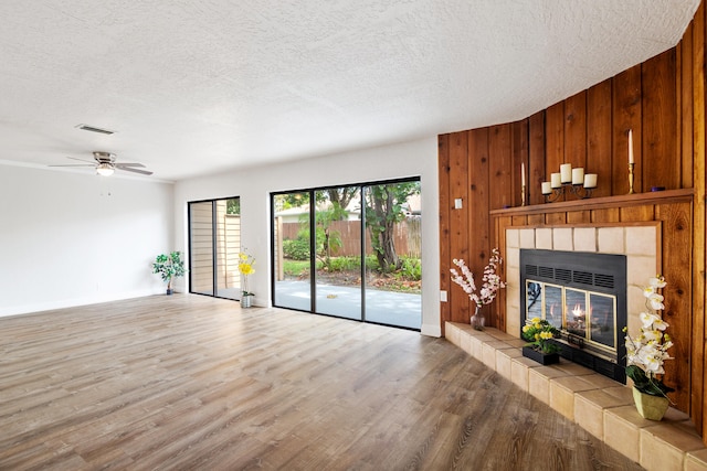 unfurnished living room featuring ceiling fan, a fireplace, a textured ceiling, wood walls, and hardwood / wood-style flooring