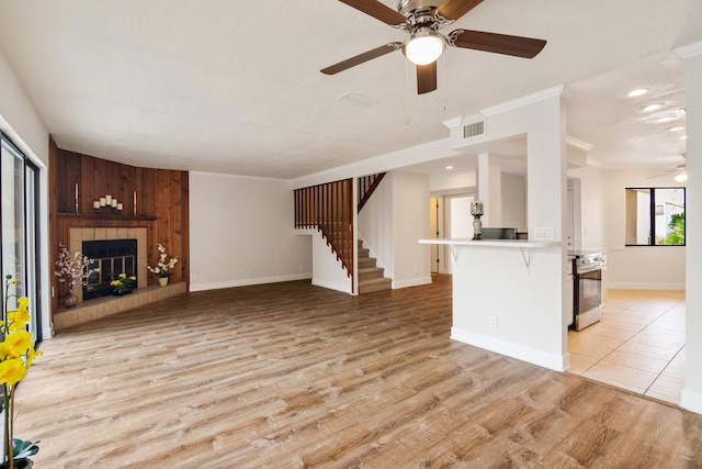 unfurnished living room featuring wood walls, ceiling fan, a tile fireplace, light tile floors, and ornamental molding