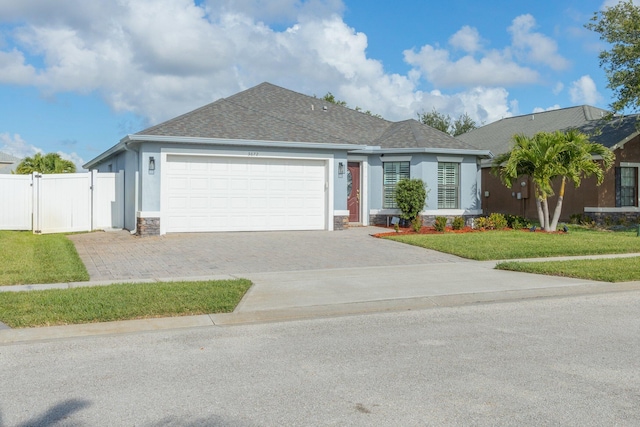 ranch-style house featuring a gate, driveway, stucco siding, a front lawn, and stone siding