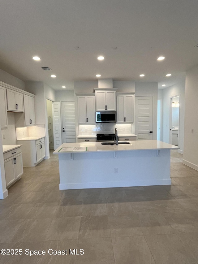 kitchen with sink, decorative backsplash, an island with sink, and white cabinets