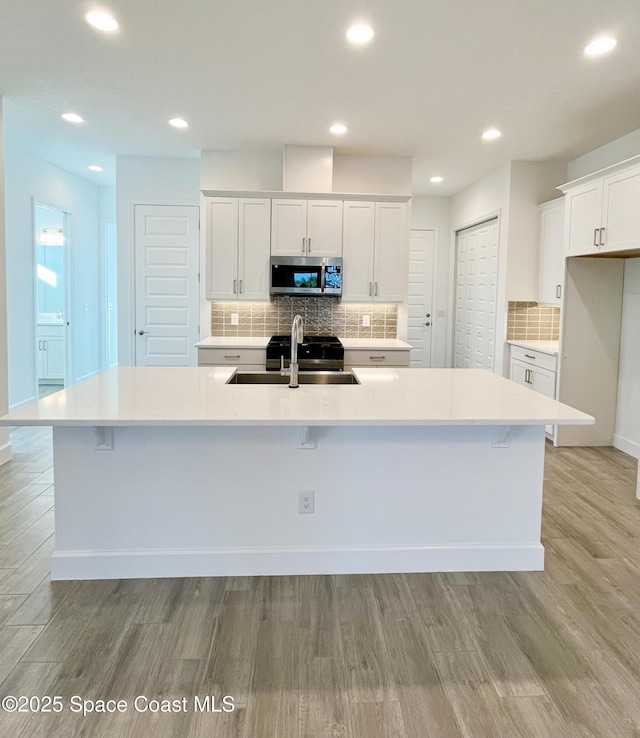 kitchen featuring a spacious island, a sink, white cabinets, light wood-type flooring, and stainless steel microwave