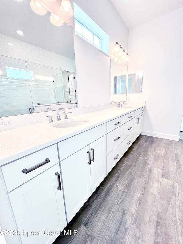 bathroom featuring double vanity, wood finished floors, a stall shower, and a sink