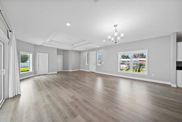 unfurnished living room featuring a raised ceiling, a textured ceiling, and an inviting chandelier