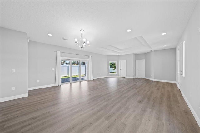 unfurnished living room featuring a tray ceiling, light wood-type flooring, a textured ceiling, and a notable chandelier