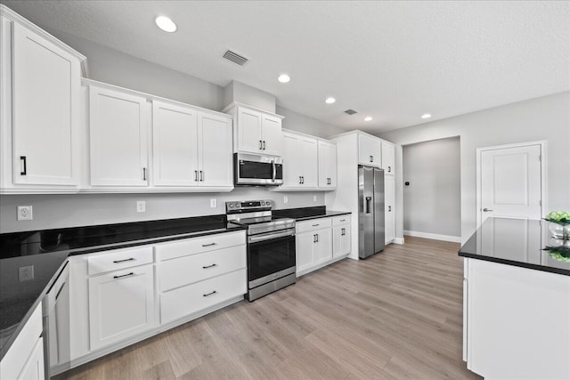 kitchen with white cabinets, a textured ceiling, stainless steel appliances, and light hardwood / wood-style flooring