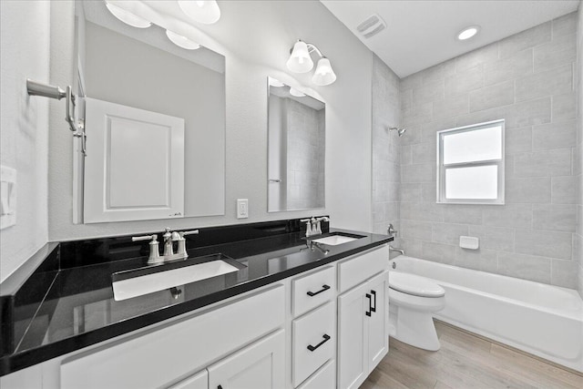 full bathroom featuring hardwood / wood-style floors, vanity, toilet, and tiled shower / bath