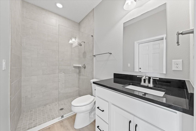 bathroom with hardwood / wood-style floors, vanity, toilet, and a tile shower