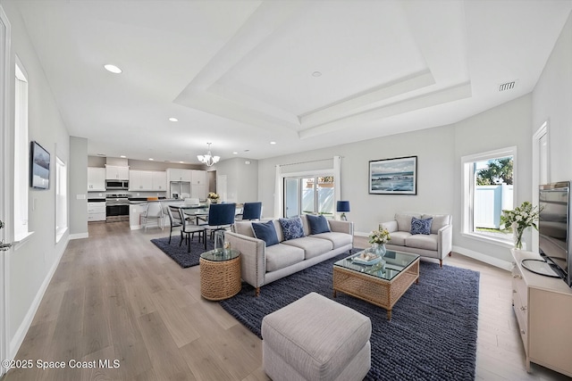 living room featuring a raised ceiling, light hardwood / wood-style floors, and a notable chandelier