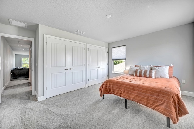 bedroom with multiple closets, carpet, a textured ceiling, and multiple windows