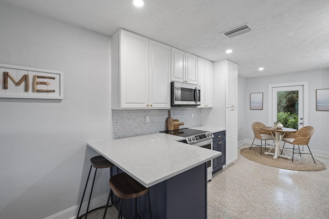 kitchen with kitchen peninsula, appliances with stainless steel finishes, backsplash, white cabinetry, and a breakfast bar area