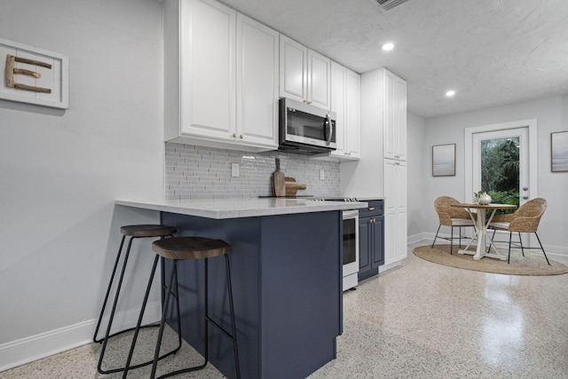 kitchen with a breakfast bar area, backsplash, white cabinetry, and stove