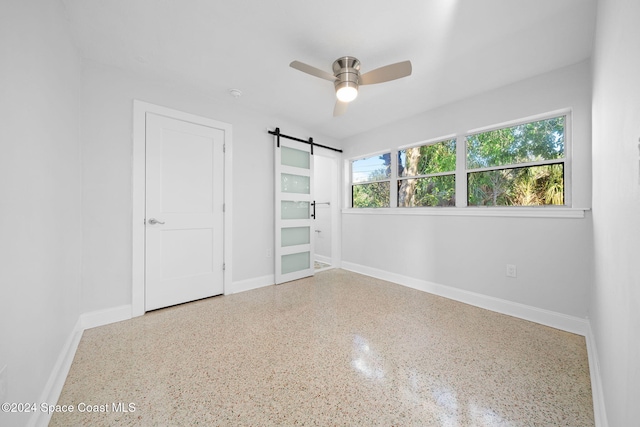 unfurnished bedroom featuring a barn door and ceiling fan