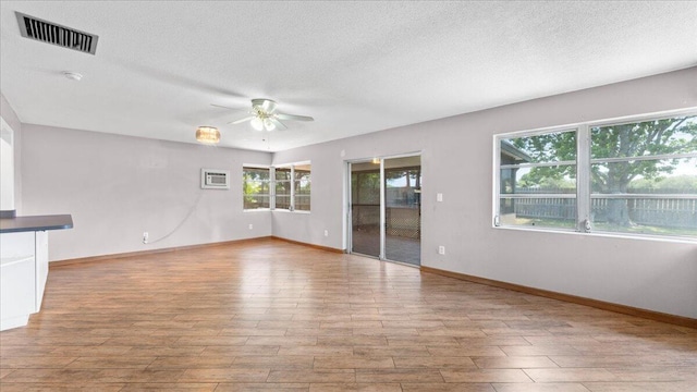 unfurnished living room featuring a textured ceiling, light hardwood / wood-style flooring, ceiling fan, and a wall unit AC