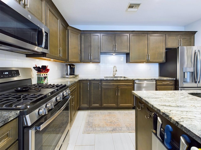 kitchen featuring stainless steel appliances, light stone counters, tasteful backsplash, and sink