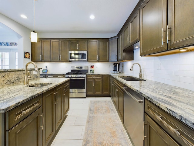 kitchen with appliances with stainless steel finishes, sink, light stone countertops, and pendant lighting