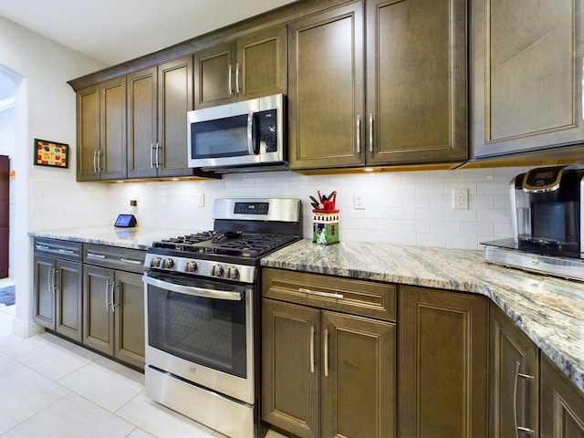 kitchen with backsplash, appliances with stainless steel finishes, light stone countertops, and light tile flooring