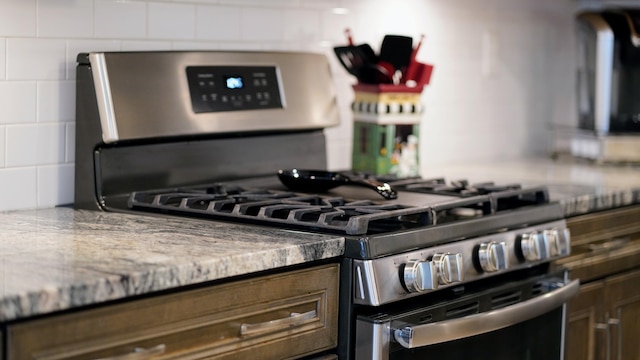 kitchen with gas range, light stone counters, and tasteful backsplash