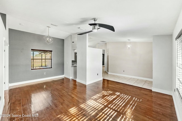 unfurnished living room with hardwood / wood-style flooring, ceiling fan with notable chandelier, and lofted ceiling