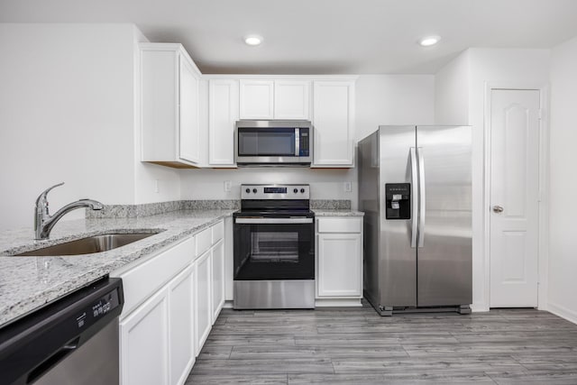 kitchen with appliances with stainless steel finishes, white cabinetry, sink, light stone countertops, and light hardwood / wood-style flooring