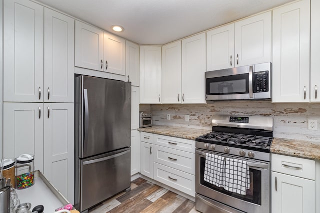 kitchen with dark hardwood / wood-style floors, decorative backsplash, white cabinetry, and appliances with stainless steel finishes