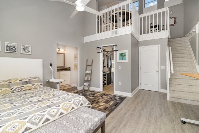 bedroom featuring a high ceiling, hardwood / wood-style flooring, ensuite bath, and ceiling fan