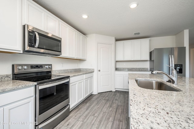 kitchen with appliances with stainless steel finishes, white cabinetry, sink, light stone counters, and light hardwood / wood-style flooring