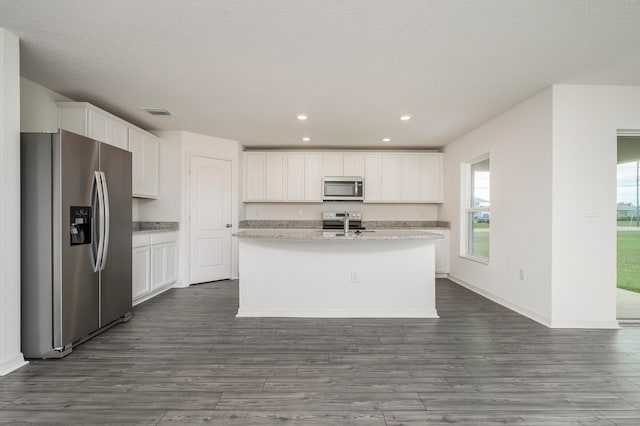 kitchen featuring stainless steel appliances, a center island with sink, white cabinetry, light stone countertops, and wood-type flooring