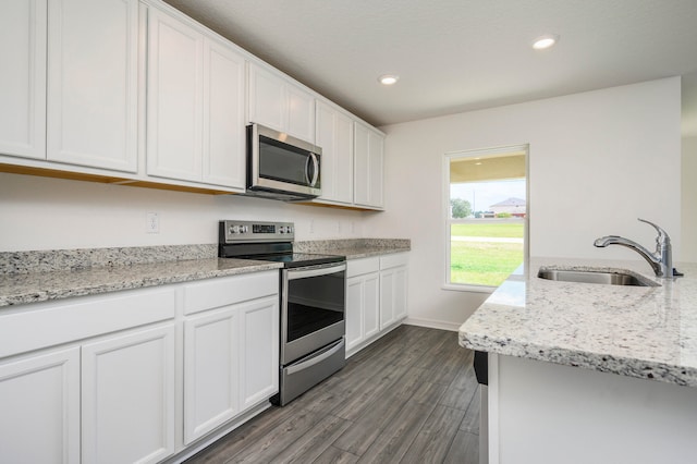 kitchen with light stone counters, stainless steel appliances, white cabinetry, dark wood-type flooring, and sink