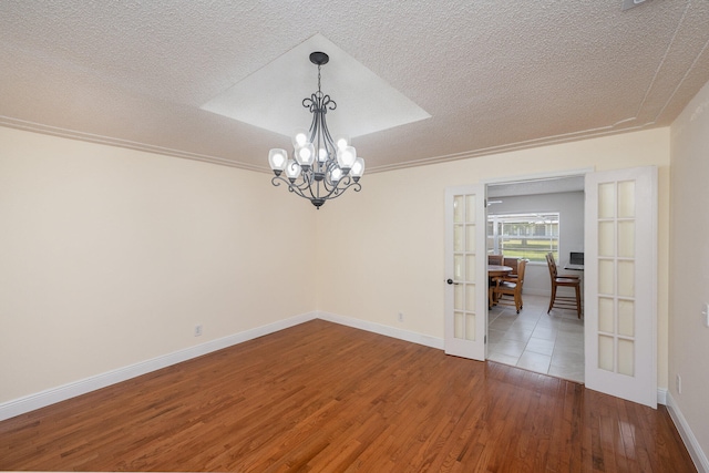 spare room with an inviting chandelier, a textured ceiling, french doors, and wood-type flooring