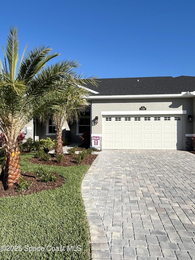 view of front facade with decorative driveway, an attached garage, and stucco siding