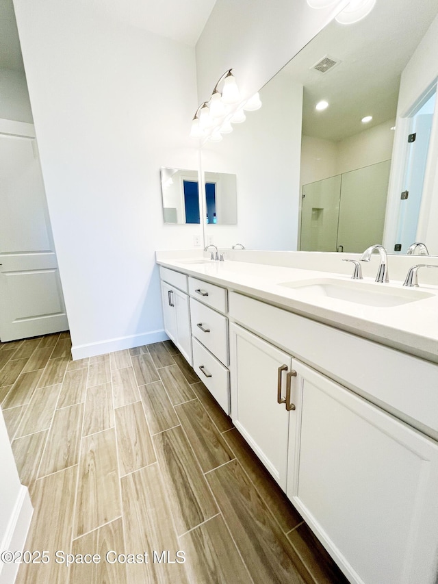 bathroom with a stall shower, wood tiled floor, visible vents, and a sink