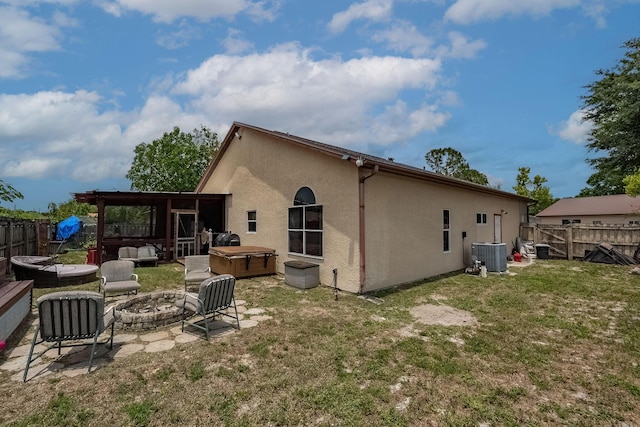 rear view of house featuring a hot tub, a fire pit, central AC unit, and a lawn