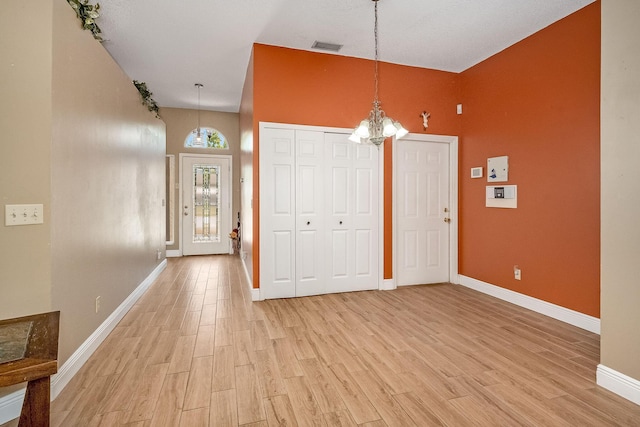 foyer entrance featuring a towering ceiling, light wood-type flooring, and a notable chandelier