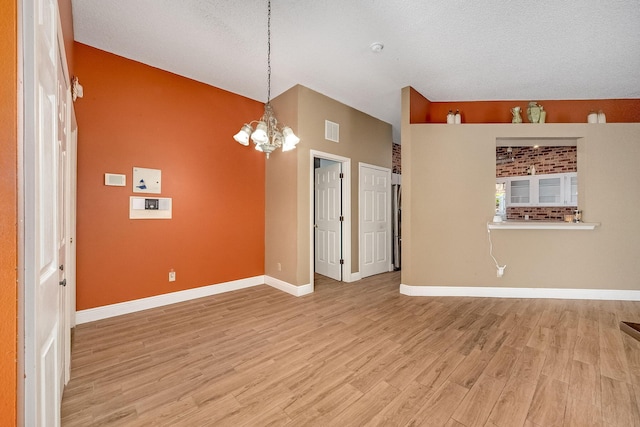 spare room with a textured ceiling, light hardwood / wood-style floors, and an inviting chandelier