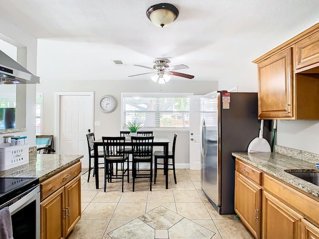 280 Monroe Ave, Cape Canaveral, FL 32920 - kitchen featuring a ceiling fan, appliances with stainless steel finishes, light stone counters, light tile patterned floors, and brown cabinetry