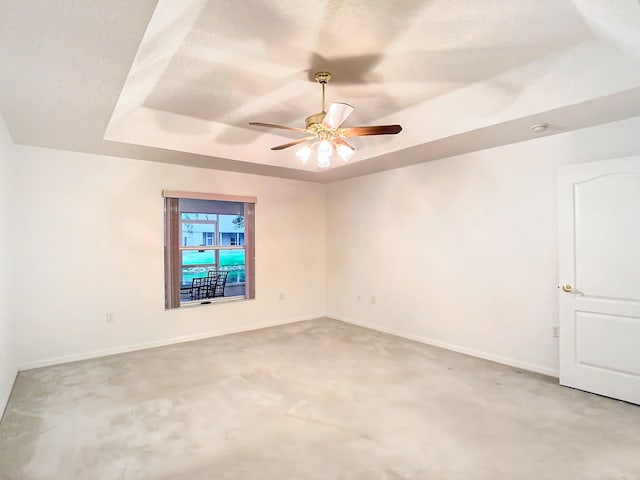 empty room with a textured ceiling, a raised ceiling, and ceiling fan