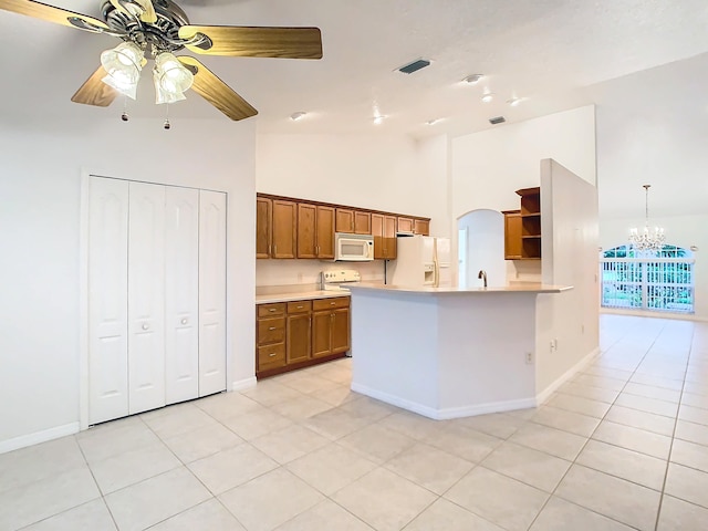 kitchen featuring light tile patterned flooring, hanging light fixtures, kitchen peninsula, white appliances, and ceiling fan with notable chandelier