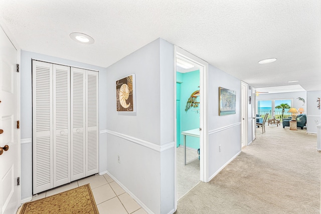 hall featuring a textured ceiling and light colored carpet