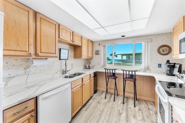 kitchen with white appliances, sink, light wood-type flooring, and light stone countertops