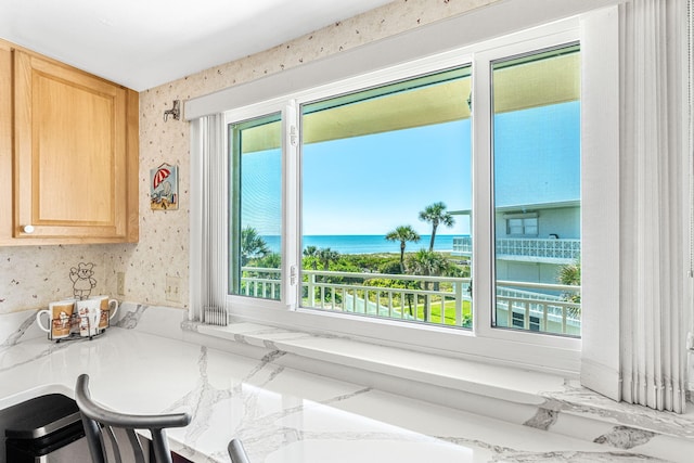 kitchen featuring light brown cabinets, a kitchen breakfast bar, a water view, and light stone countertops