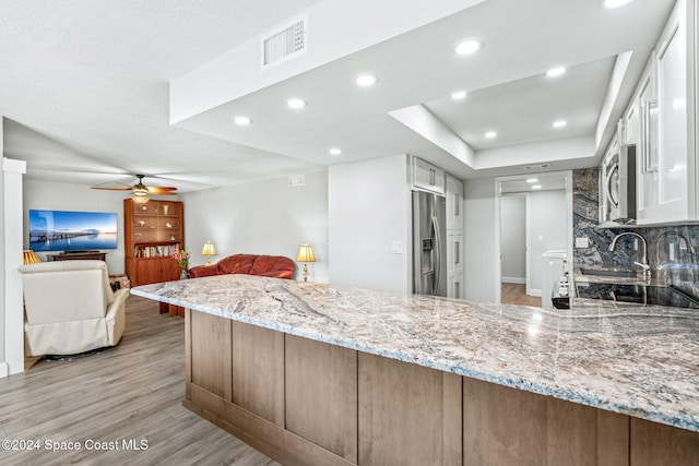 kitchen with tasteful backsplash, light stone countertops, kitchen peninsula, stainless steel appliances, and light hardwood / wood-style flooring