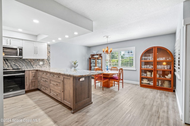 kitchen featuring appliances with stainless steel finishes, light hardwood / wood-style flooring, white cabinets, and a notable chandelier