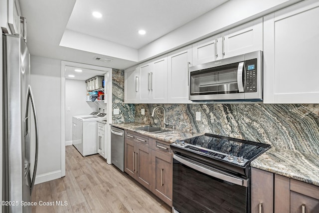 115 N Indian River Dr Unit 133, Cocoa, FL 32922 - kitchen featuring appliances with stainless steel finishes, a sink, washing machine and dryer, light wood-style floors, and white cabinets