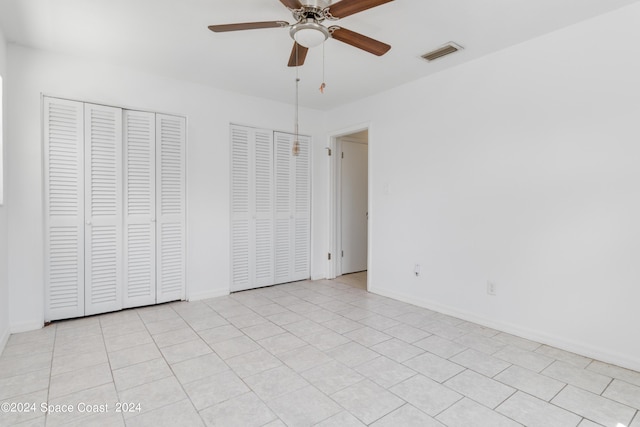 unfurnished bedroom featuring ceiling fan, light tile patterned floors, and two closets