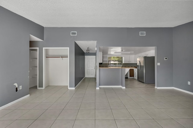 kitchen featuring stainless steel fridge with ice dispenser, white cabinets, light tile floors, and a textured ceiling