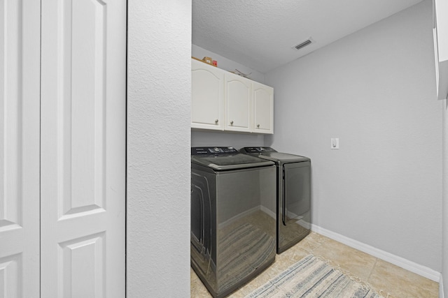 laundry area with independent washer and dryer, a textured ceiling, light tile floors, and cabinets