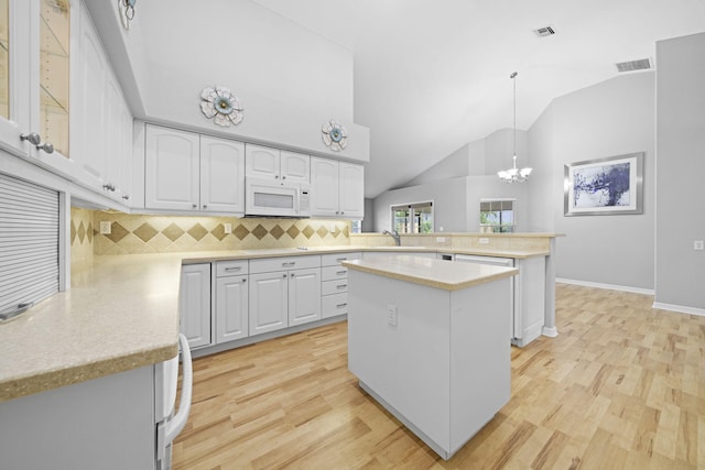 kitchen with white cabinetry, light wood-type flooring, a kitchen island, kitchen peninsula, and tasteful backsplash